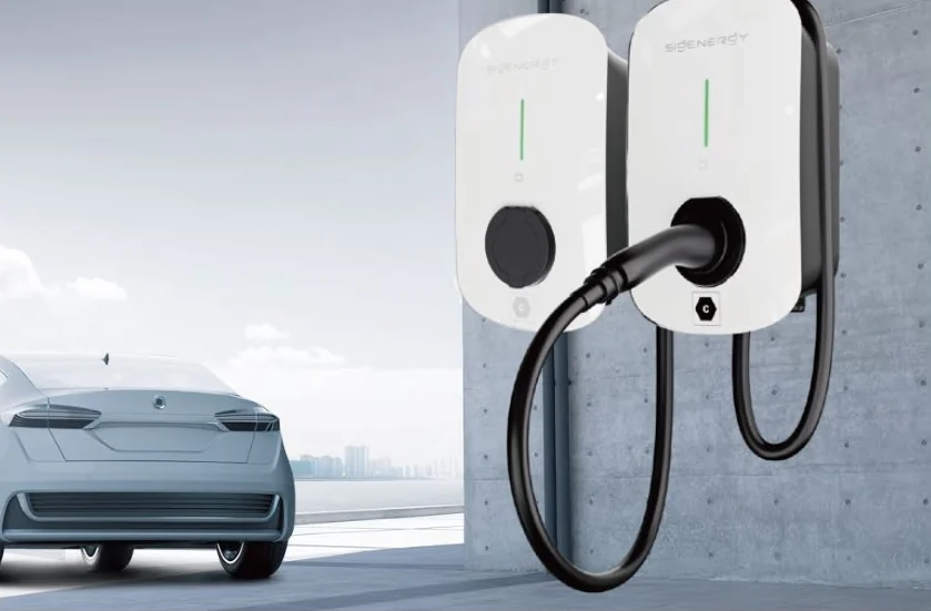 Two SigEnergy AC EV chargers mounted side by side on a concrete wall, one with its cable plugged in and hanging coiled, a car parked alongside