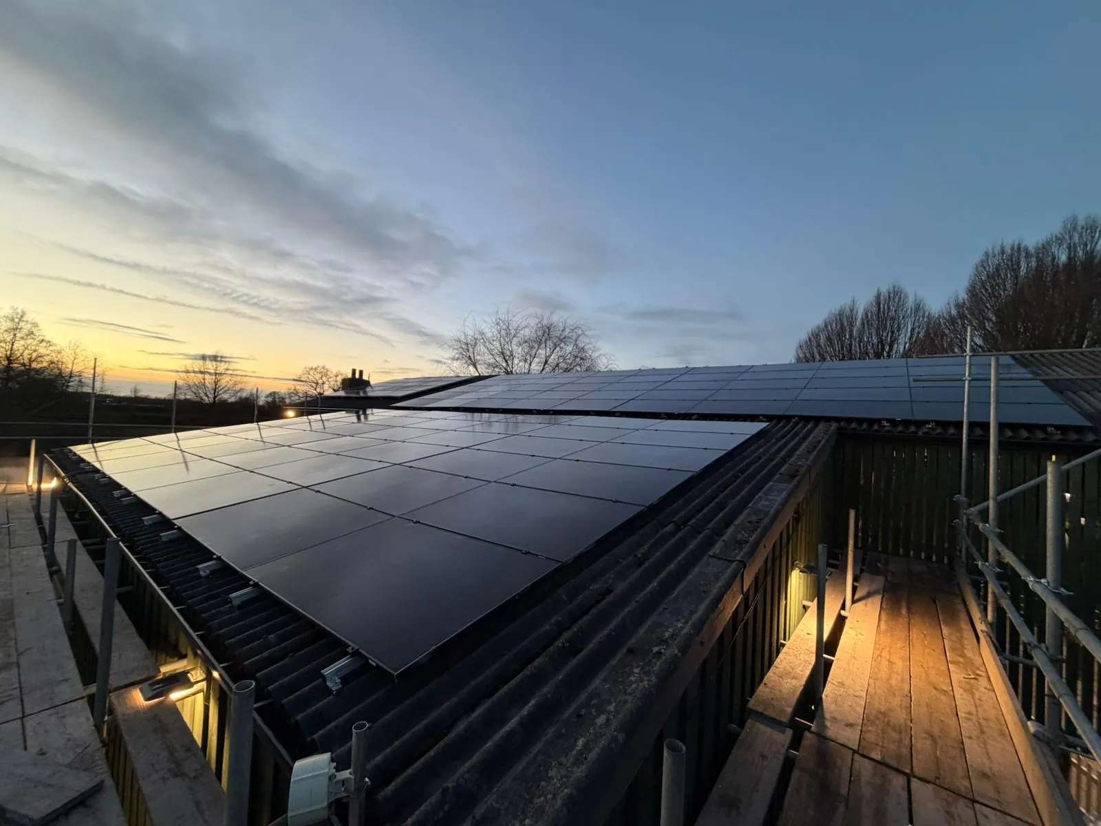 Solar panels on a barn roof at dusk, scaffold still up and worklights on